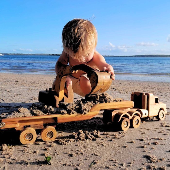 Big luxury Handmade Wooden Toy Excavator Digger. Heirloom. Durable. Functional Arm, boom, blade. Rotating Cab. pre-school boy playing with digger, digging sand on beach and loading onto handmade wooden truck.