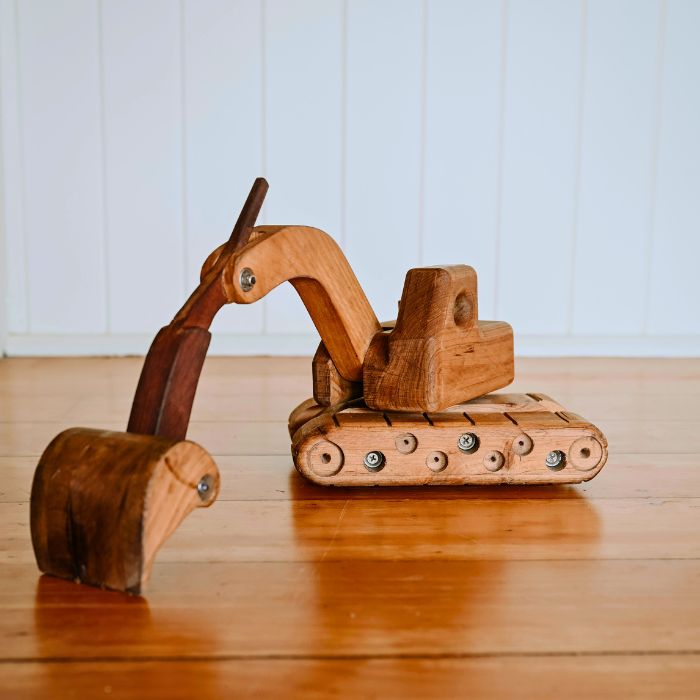 A big durable wooden excavator toy showcasing rotating cab and functioning arm boom and bucket capabilities. Rugged tread with rolling wheels beneath.