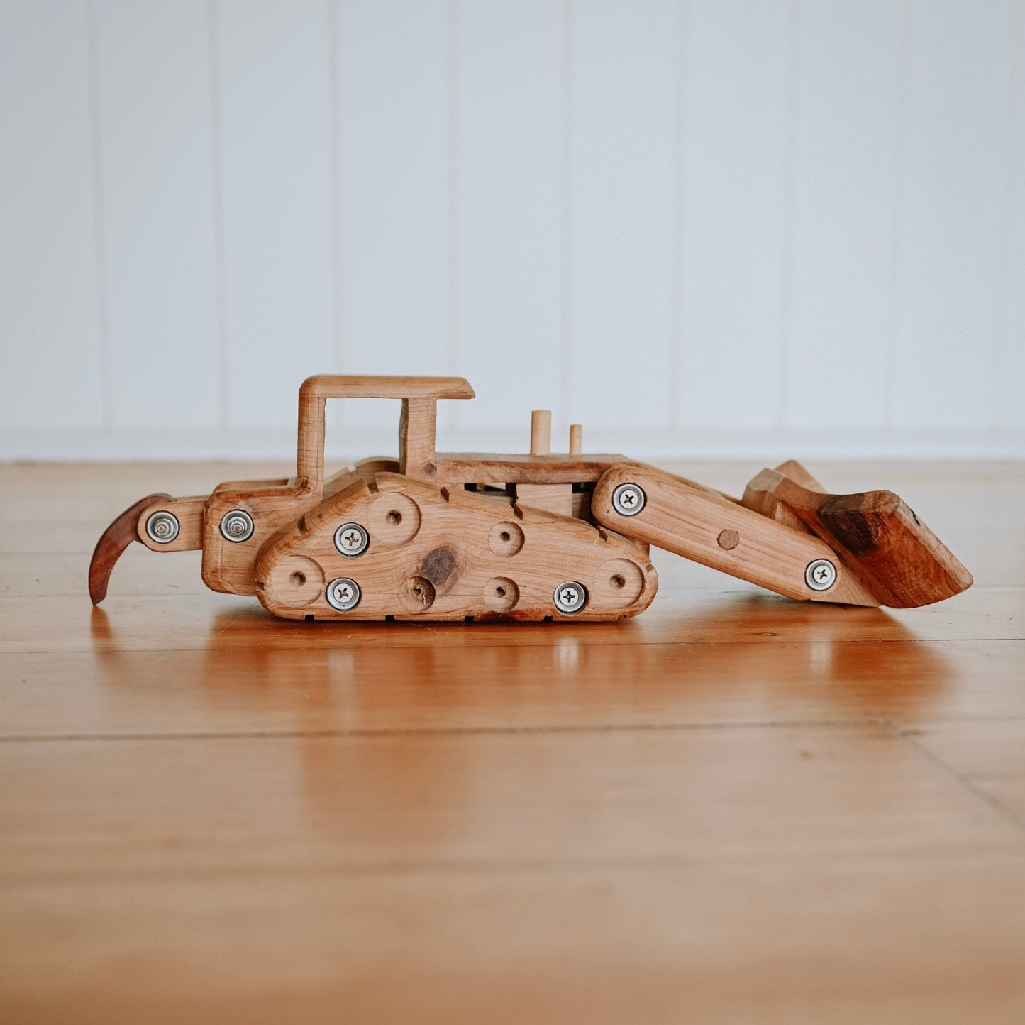 Exclusive Handmade wooden Bulldozer, placed on luxurious floorboards. Showcasing intricate details, quality craftmanship and functional ripper and blade. Heirloom quality