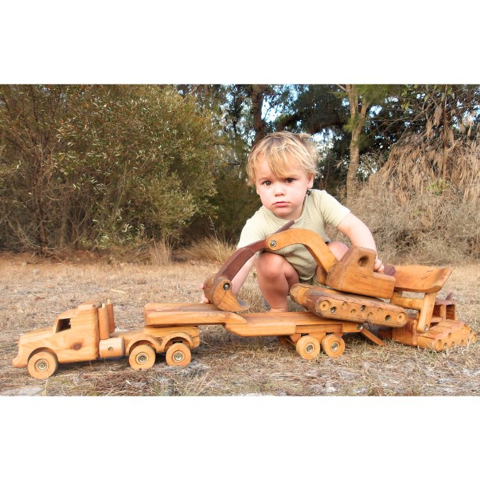 Pre-school boy playing outside with premium handmade wooden construction toy set. Unloading Bulldozer and digger from float trailer on back of low loader truck. Showcasing imaginative and roll play