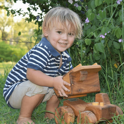 A happy pre-school boy playing outside with his quality handmade wooden dump truck. Smiling as he lifts the dump body. 