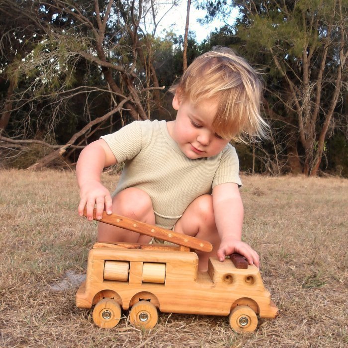 A 3 year old boy playing outside with handmade wooden fire truck. Showcasing imaginative play with removable ladder and rolling wheels