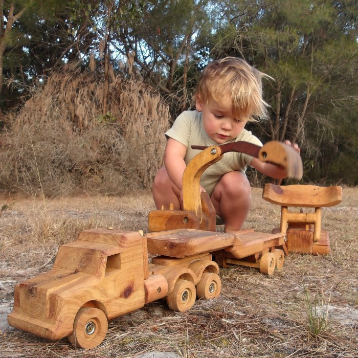 A 3 year old boy playing with huge quality construction toy set. Durable truck and float trailer functional boom of excavator and dozer blade raised.