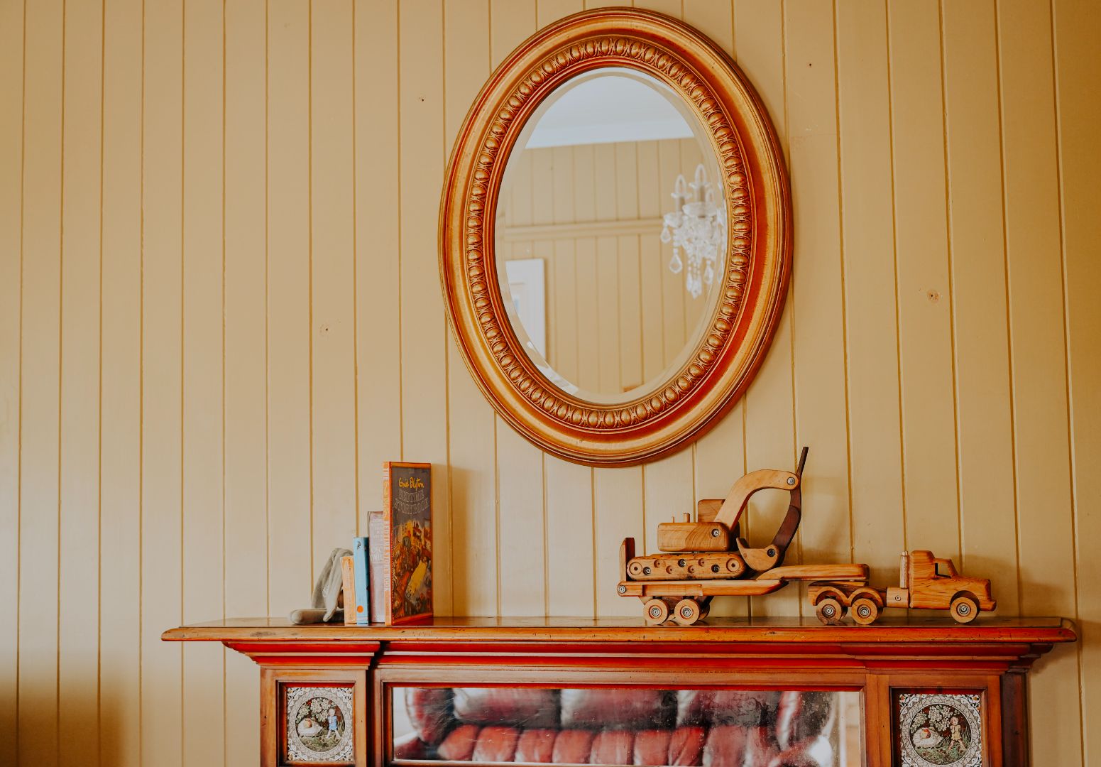 Luxury Old Money Country decor, styled with premium wooden construction vehicles and classic children's books as centrepieces on timber mantle. Gold mirror and chesterfield in reflection.