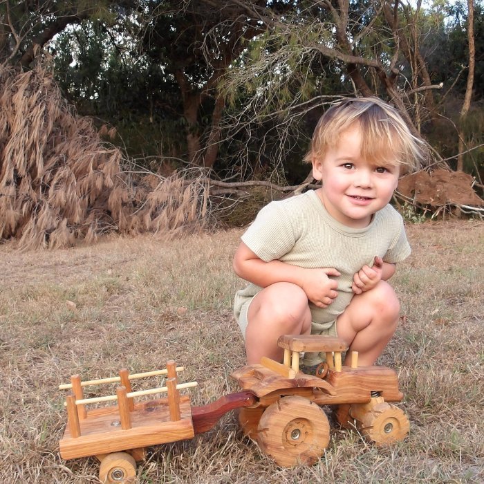 Toddler Boy happily playing with Handmade Wooden Tractor Trailer Toy in Australian Bush. Showcasing premium features such as Removable Trailer. Suspension. Rolling Wheels. Push pull. Durable Quality. 